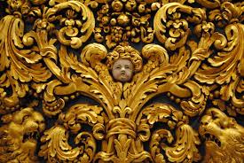 Baroque style art detail in gold with flourishes and an angel head in the center. 