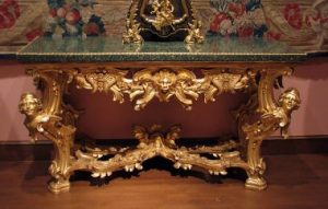 A table with gold, ornate legs and a glass top in the Baroque style. 
