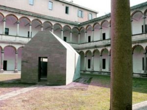 Casa di Pietra nel Salone del Mobile a Milano, 2010. Piccola casa di pietra al centro di un cortile di un palazzo che presenta due piani decorati con archi. 