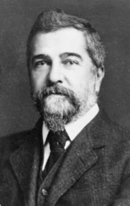 Photo of Tiffany from 1908: A man with an expressionless face, a large scruffy beard and wearing a nice jacket and tie.