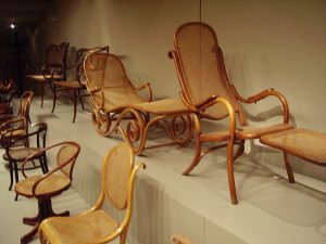 A photo of Thonet bentwood chairs in a warehouse-like setting. The chairs are a light wood with a weave seat and backing. 