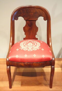 A medium-wood gondola chair with a red cushion adorned with white flourish details. 