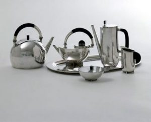 Tea kit by Marianne Brandt: A six piece tea kettle set in a shiny, silver colored metal. 