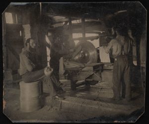 Intérieur d'un moulin montrant trois hommes utilisant une scie circulaire, Maberly, Ontario.