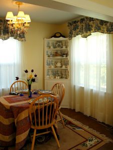 French Country Style Interior: A photo of a dinning room with white curtains, a light wood dinning set and a cute little chandelier. 