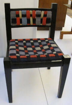 Gunta Stölzl textiles on a Marcel Breuer chair (1922): A checkered cushioned chair with dark wood legs. 