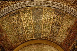 Mosaicos das aduelas do arco do Mihrab em estilo omíada. Os mosaicos são dourados e compostos por florescências em forma de folha. 