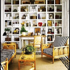 Boho interior photo with a collage-like bookcase and whicker chairs with black and white stripped pillows
