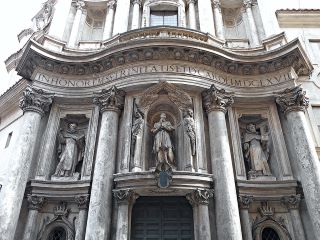 Facciata della Chiesa di San Carlino alle Quattro Fontane a Roma. Una grande struttura in pietra chiara con tre statue al centro e 4 colonne lungo il fronte. 
