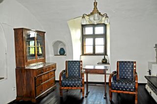 Roménia, sala de estar de estilo Biedermeier com paredes brancas, cadeiras de madeira escura com almofadas azuis e um armário de madeira escura. 