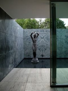 Estátua no Pavilhão Mies van der Rohe feita de material opaco escuro, representando uma mulher nua com os dois braços sobre a cabeça. 