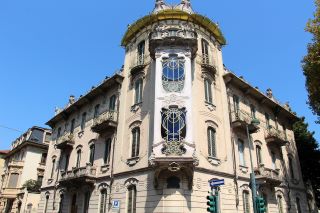 Casa Fenoglio: Um grande edifício luminoso com janelas ornamentais e uma torre de canto central. 
