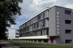Edifício Bauhaus em Dessau, com fachada cinza e um lado do edifício com uma fachada coberta por uma grade de metal. 