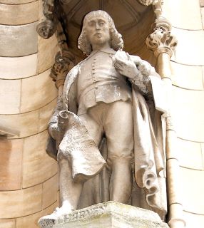 Estátua de Sir Isaac Newton em pedra de cor clara. Newton aparece com um manuscrito numa mão, apoiado numa perna. 