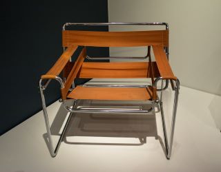 Sedia Wassily, Design Funzionale con essenziale struttura in metallo e pezzi di tessuto marrone per ricoprire la seduta, lo schienale e i braccioli. 