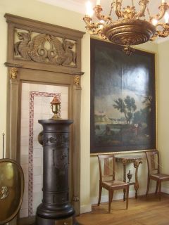 Salão Directoire do Museu Couven. Um exemplo do estilo Directoire com um grande quadro à direita, um lustre dourado e duas cadeiras em tons de castanho, Estilo Directório.
