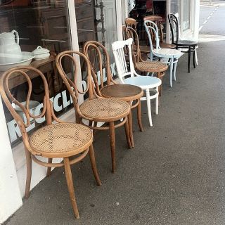 Diversi modelli di sedie di legno disposte in fila, in primo e in secondo piano. 