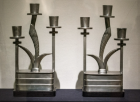 Two candelabras with three candles each, both in a dark metal. 