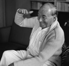 Alvar Aalto photo where he is smiling and holding his right-hand flat at about eye-level. Additionally, the photo is in black and white. 