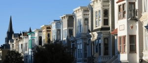 A strip of Edwardian houses in San Francisco; the downtown in the background. All the homes vary in color, although pastels seem to be most common. 