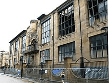 Glasgow School of Art, designed by Charles Rennie Mackintosh: A photo of a light stone building with black windows. 