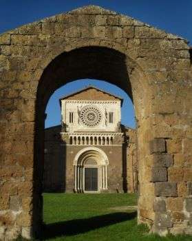 Photo of St. Peter's Dome, located in Tuscania, seen from the outside. An arch made of bricks enframes the facade of the Dome.