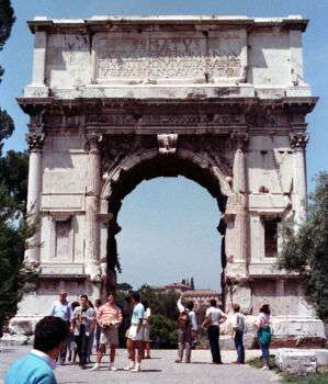 The Arch of Titus (IV): a single stone arch that stands 15 meters, with various tourists surrounding the base. 