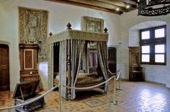 King Henri II's Chamber: A lavish canopy bed sits in the center, with tapestries on either side, a window and a chair on the right side of the room. 