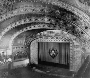 Auditorium Theatre interior from the balcony, Adler & Sullivan (1889). Photo in black and white. A grand ceiling with a large stage and various people in the audience. 