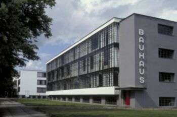 A Bauhaus style building with a grey facade and a side of the building with a gated-facade. 