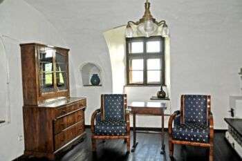 Biedermeier Salon with plain wall, dark wood chairs with blue cushions and a dark wood wall cabinet. 
