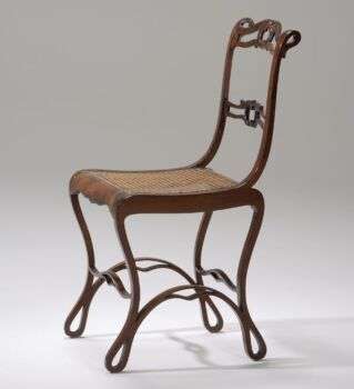 Una sedia sinuosa con gambe e schienale sottili. La seduta è realizzata in un legno in stile intrecciato. 