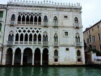 The Ca' d'Oro located in Venice, Italy. This structure is a three tiered structure with skinny arches and a fence that lines the top of the structure. Moreover, it is located on the Grand Canal. 