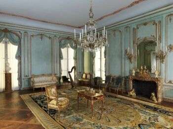  The interior view of a very fancy house. The walls are a light blue with gold accents, there is a large chandelier in the center, a large, intricate rug on the ground and various gold-accented furniture around the room. 
