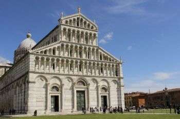 Picture of the Pisa Cathedral, in Tuscany. A great lawn stretches in front of the Cathedral, with dozens of tourists waiting in line to enter. 