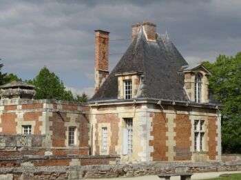 Château d'Anet de style Renaissance shown from a differing angle. It has a dark roof and light, mixed stone walls.

