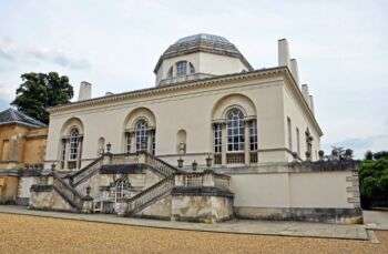 Chiswick House shown from the back. A grand, curvy staircase comes out from the left and right of the central arched door in the center. 