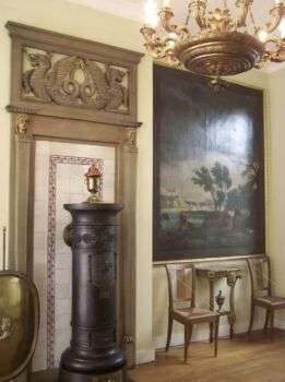 An example of Directoire style with a large painting on the right, a gold chandelier and two chairs. 