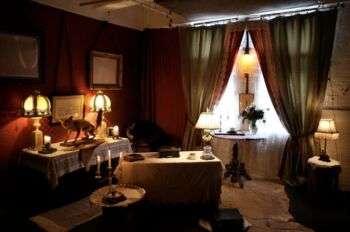Exemplo de mobiliário renascentista inglês. Paredes vermelhas, cortinas verdes e candeeiros quentes ocupam a maior parte do quadro. 