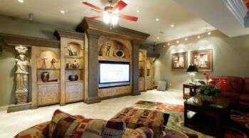 Skyline Drive Basement Entertainment Center: A tan built-in on the left with a tv in the center and various chairs and tables on the right. 
