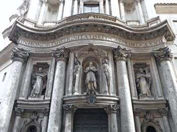 Front of San Carlo alle Quattro Fontane Church in Rome, which is a big light stone structure with three statues in the center and 4 columns along the front. 