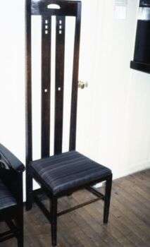 Dark wood chair with a very tall seat, and a black cushion. 
