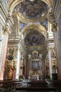 Interior photo of Chiesa Nuova in Rome. A gold-accented double domed room with various religious imagery.