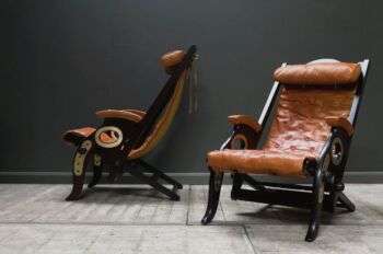 Photo of two folding chairs with brown leather backs, and dark wood structures. 