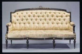 A pale yellow sofa with a maple wood base. Additionally, it is adorned with bronze flourishes. 