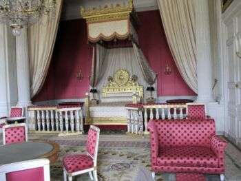 Louis XIV's Bedroom with pink poka-dotted furniture and a large, white bed with gold accents. 