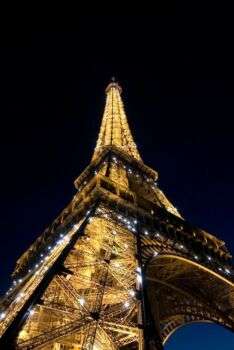 Foto della Torre Eiffel da terra, è notte e la torre scintilla di luci. 