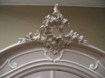 The top flourish of a white and pink Rococo armoire.