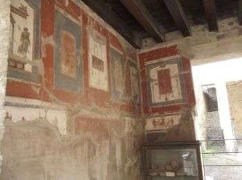Herculaneum - Casa del Colonnato Tuscanico: example of the marble-like paintings. There are rectangles of blue, red and white that occupy the top half of the wall. 