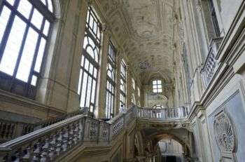 Escalier monumental de Juvarra, 1718-1711 dans le Palazzo Madama, Turin (10). De grandes fenêtres en arches bordent le côté gauche de la photo où un escalier commence et enveloppe le côté central droit de la photo. 